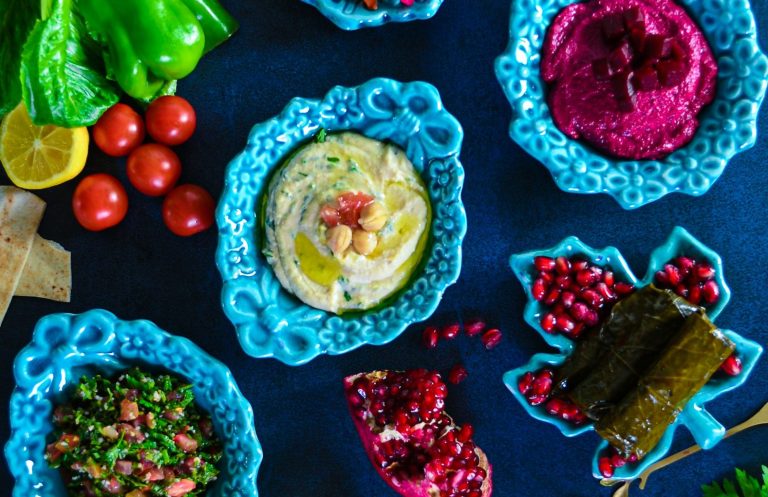 Bunte Auswahl an Dips, Gemüse und Granatapfel, serviert in blauen Schalen.