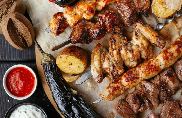 Ein Teller mit gegrilltem Fleisch, Kartoffeln, einer Sauce und eingelegtem Gemüse.